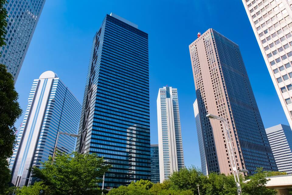 A cluster of modern skyscrapers with reflective glass facades, surrounded by lush green trees.