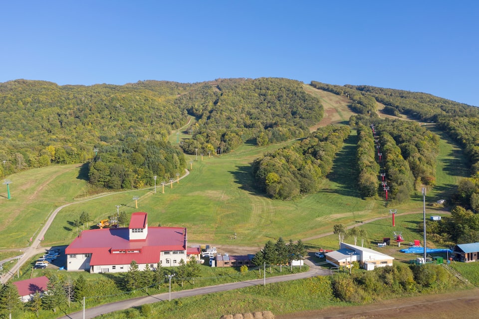 Paisagem rural com um edifício de telhado vermelho, uma estrada sinuosa e uma colina com uma trilha.