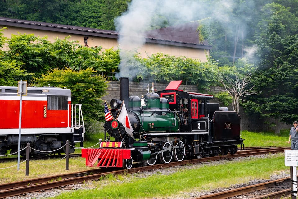 A steam locomotive with a red and black engine, number 3, on a track with a red caboose.