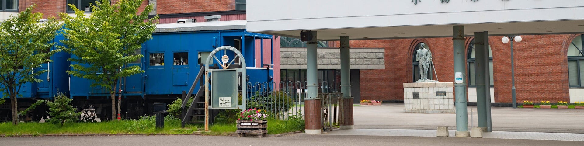 A train station with a blue locomotive, a statue, and a brick building with arched windows.