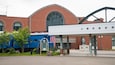 A train station with a blue locomotive, a statue, and a brick building with arched windows.