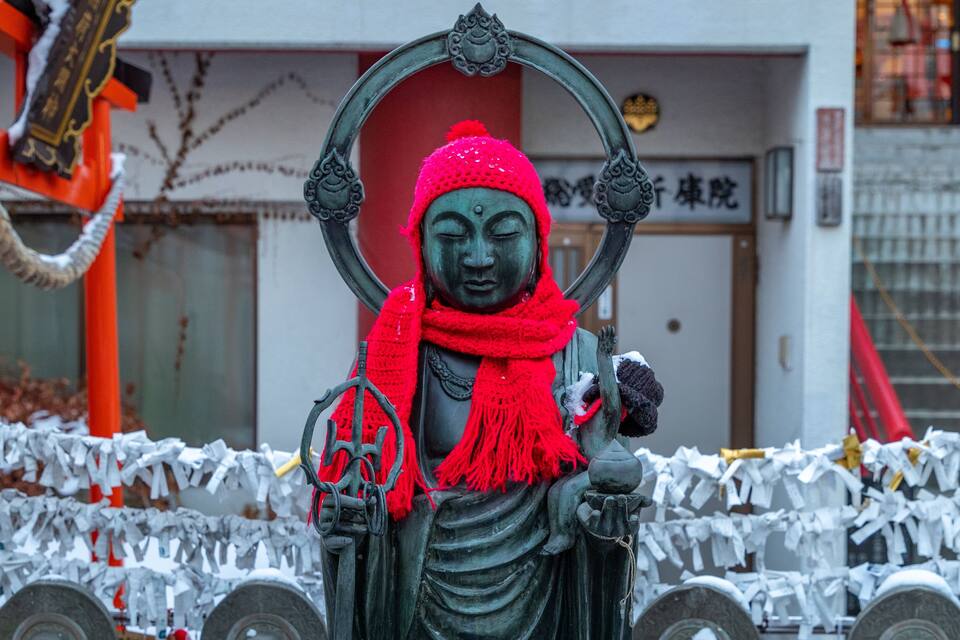 A statue of a figure with a red scarf and a halo, surrounded by white paper decorations.