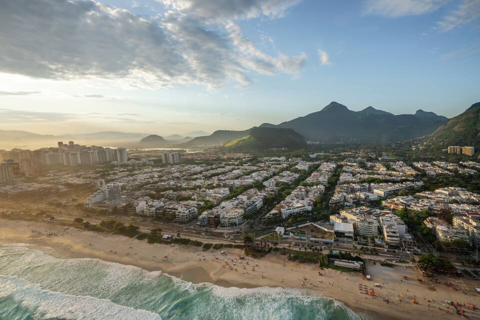 A coastal cityscape with a beach, residential buildings, and mountains in the background.