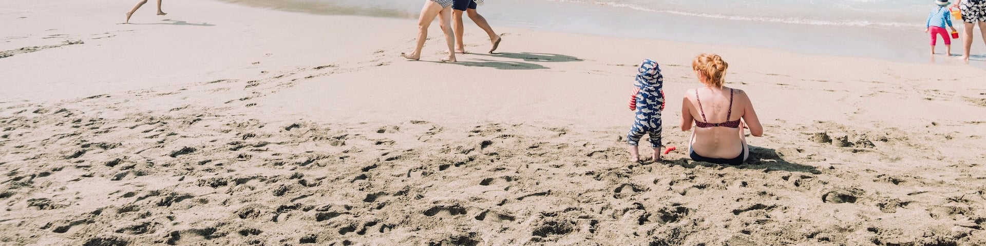 A beach with people walking and swimming, rocky cliffs, and clear blue water.