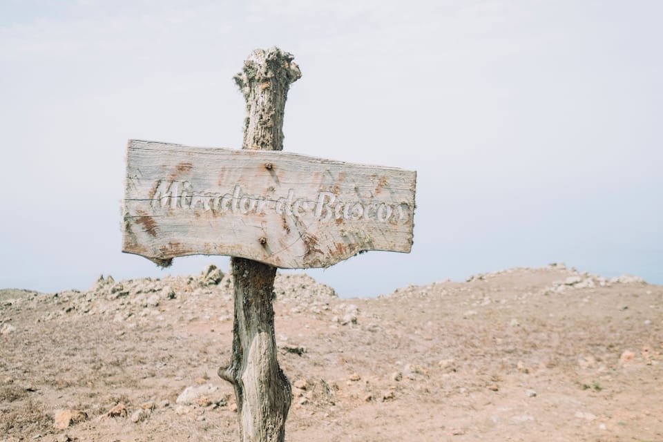 A weathered wooden signpost with the inscription "Minardos Bascom" in a rugged, rocky landscape.