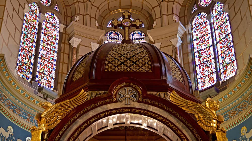 L’intérieur d’une cathédrale, avec ses vitraux, une grande croix et des décorations dorées élaborées.