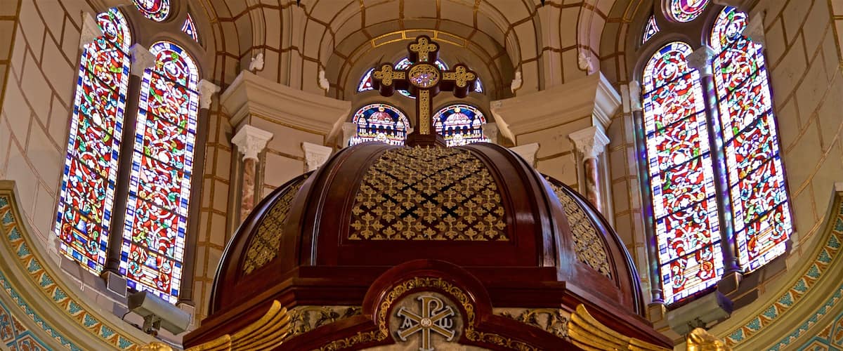 A cathedral interior with stained glass windows, a large cross, and ornate gold decorations.