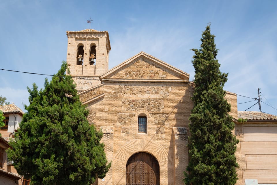 Una iglesia histórica con un campanario, ventanas de arco y una gran puerta de madera.
