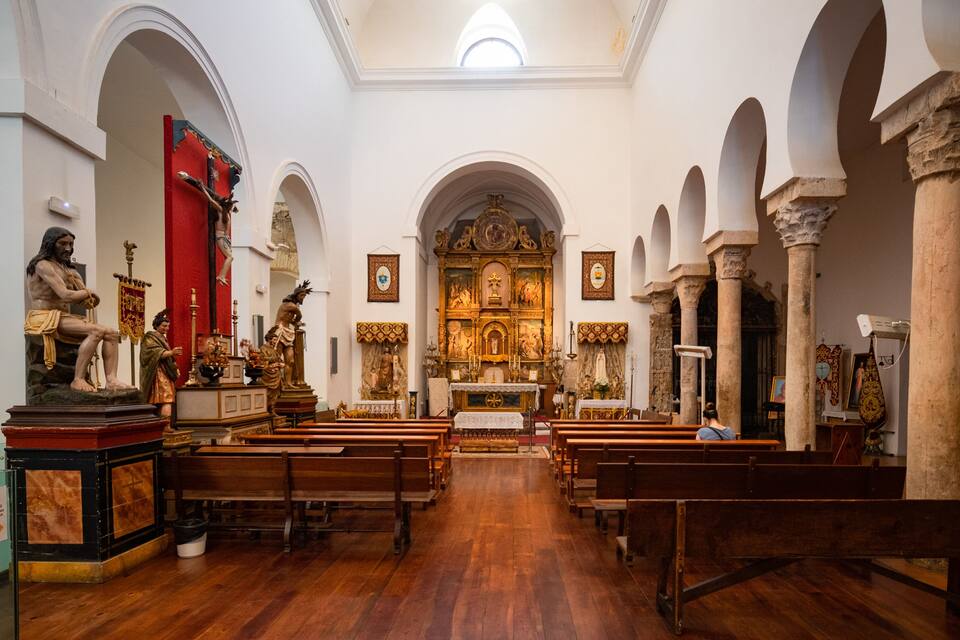 Ein Kircheninneres mit Holzbänken, Statuen und einem Altar.