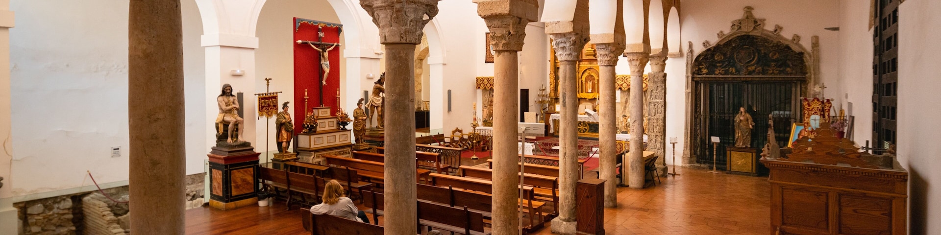 Interior de igreja com bancos de madeira, colunas de pedra e estátuas religiosas.