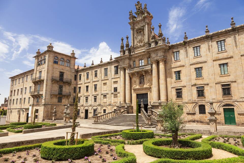 Um edifício histórico com arquitetura elaborada, uma escadaria imponente e jardins bem cuidados.