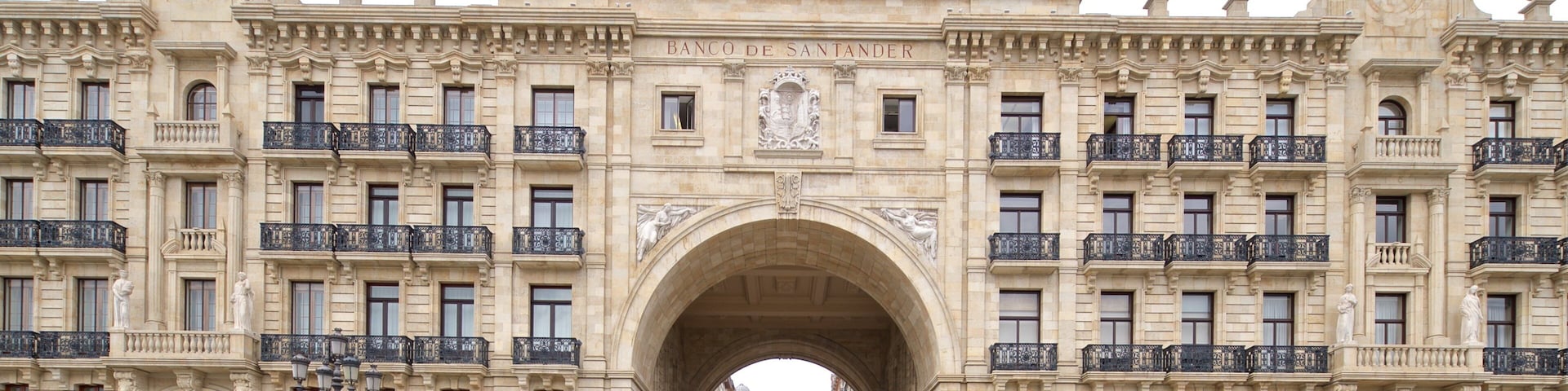 Un arco monumental con la inscripción "Banco de Santander" en la parte superior, flanqueado por edificios ornamentados con balcones y estatuas.