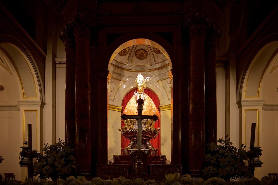 An ornate religious altar with a central statue, flanked by columns and floral arrangements.