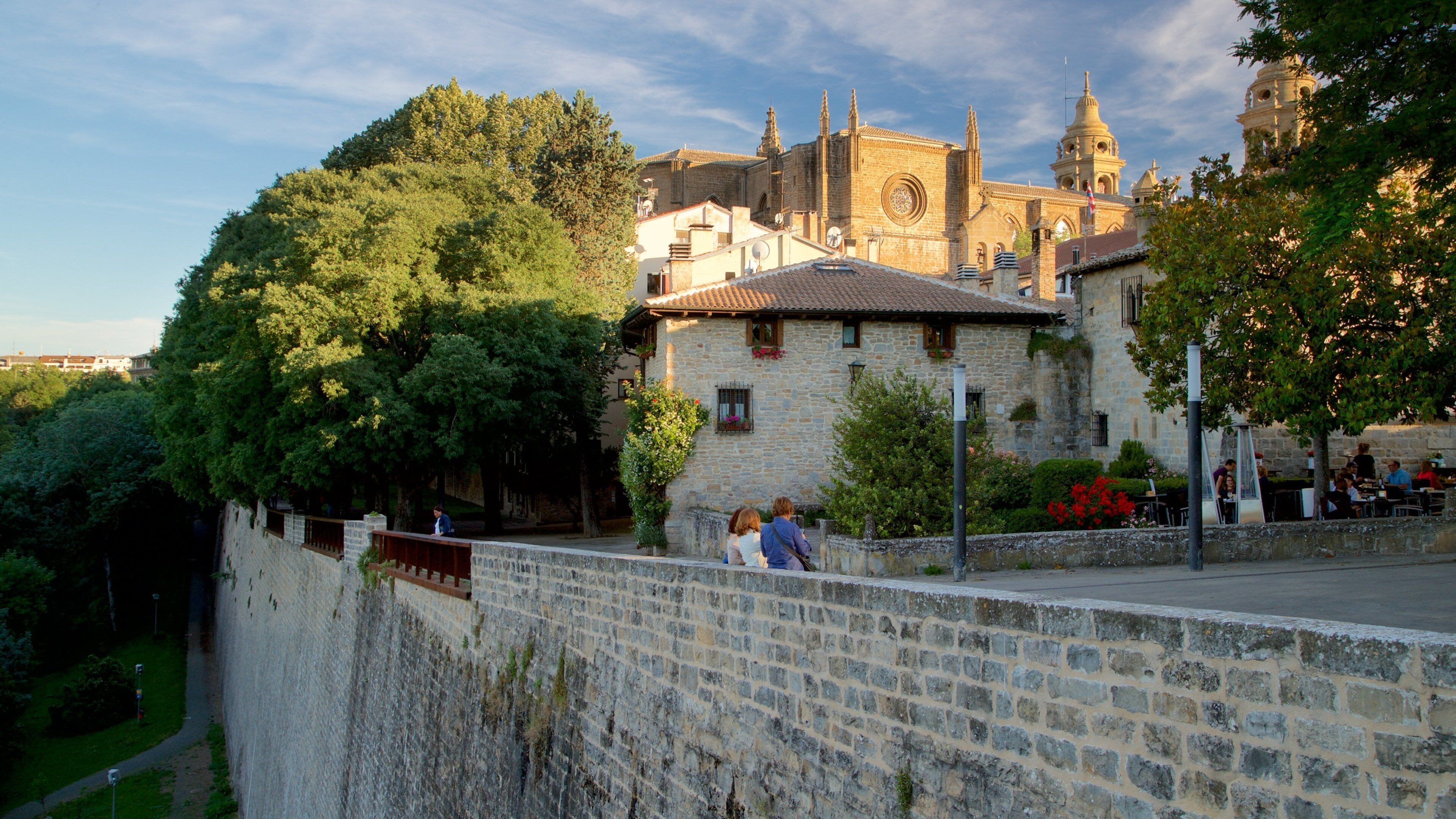 A historic stone wall, a church with a bell tower, and lush greenery.
