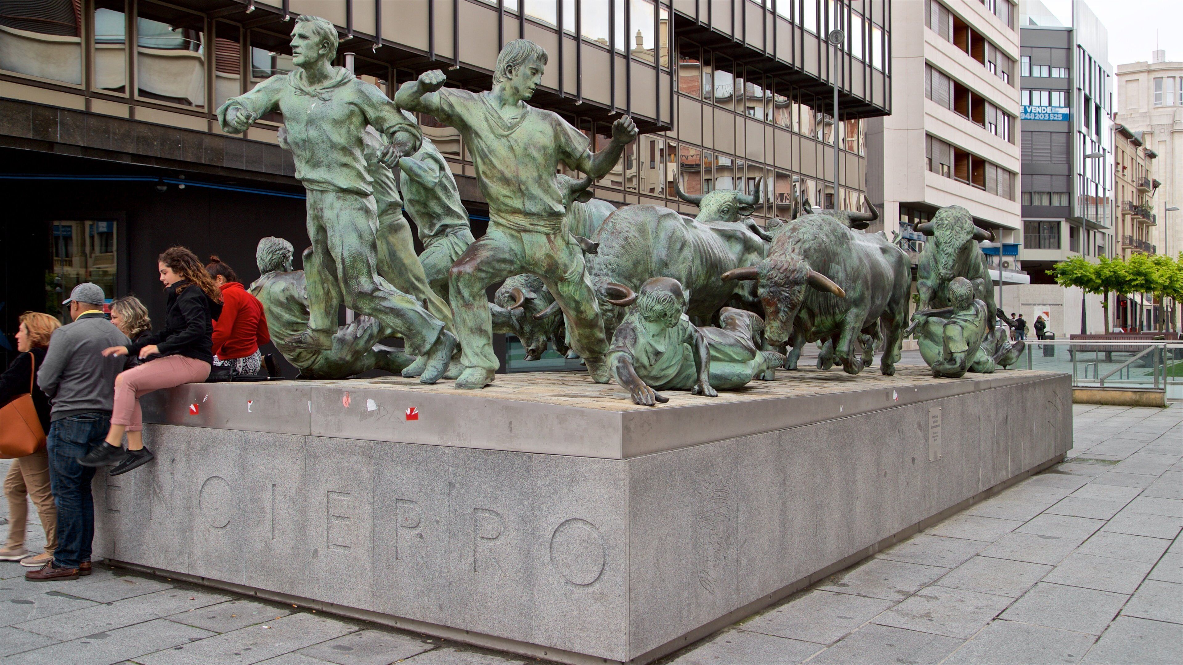 Monumento al Encierro que incluye una estatua o escultura y también un pequeño grupo de personas