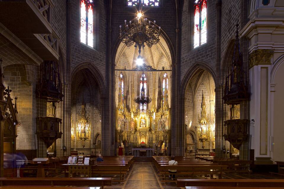 Een kathedraalinterieur met hoge gewelfde plafonds, glas-in-loodramen en versierde kroonluchters.
