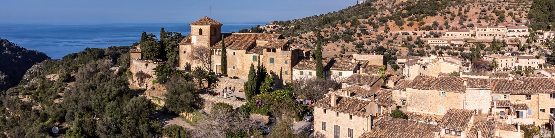 A coastal village with stone buildings, a prominent tower, and a view of the sea.