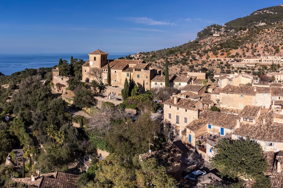 A coastal village with stone buildings, a prominent tower, and a view of the sea.