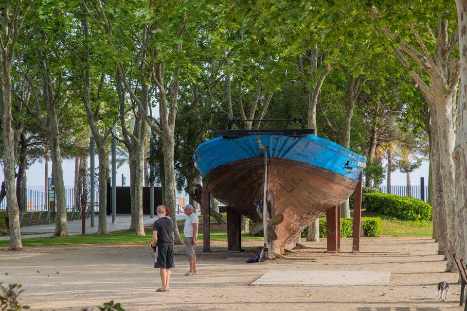 A large boat on display, surrounded by trees and a paved walkway.