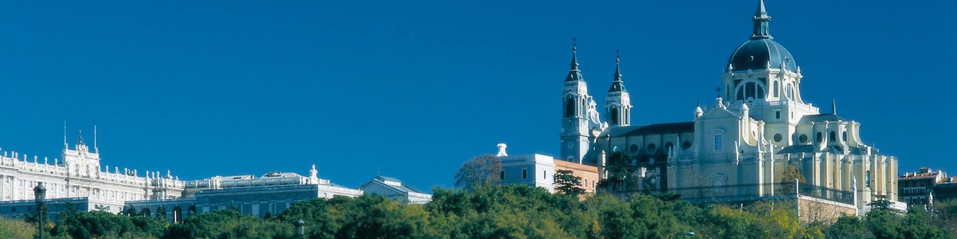 Un puente de piedra con arcos, una gran catedral con cúpulas y un paisaje urbano al fondo.