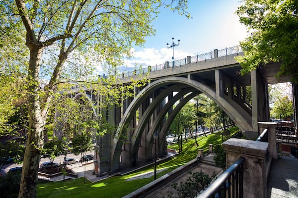 A stone bridge with arches, surrounded by trees and a well-maintained lawn.