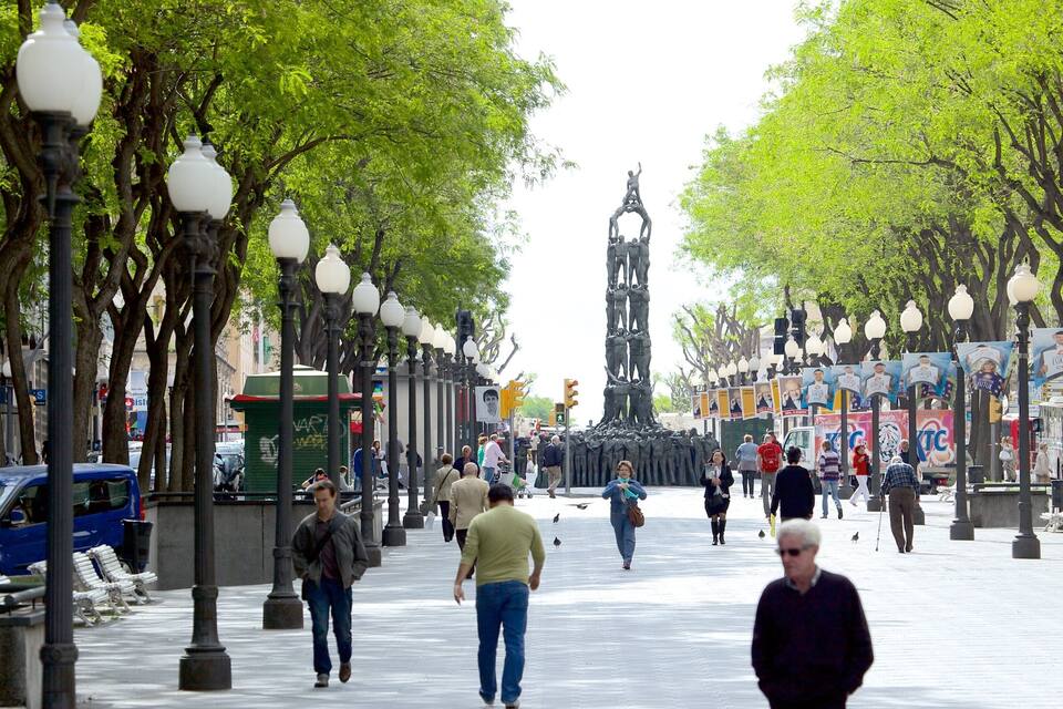 A tree-lined pedestrian street with lampposts, benches, and people walking.
