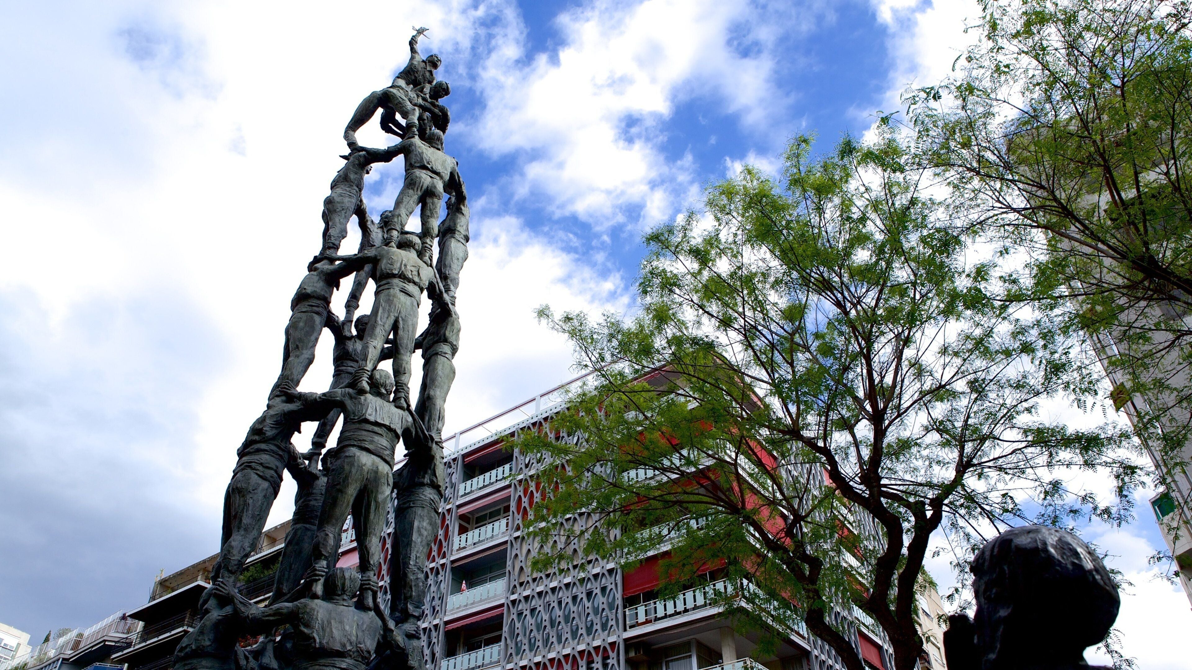 Una estatua de bronce de gran tamaño muestra soldados ascendiendo una estructura, con un edificio y árboles al fondo.