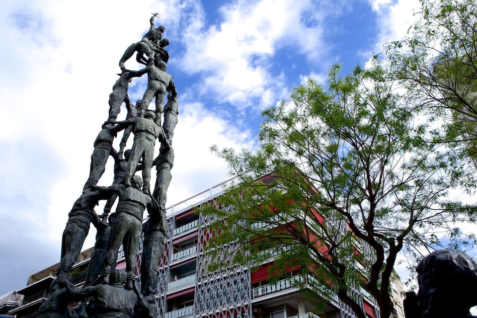 Una estatua de bronce de gran tamaño muestra soldados ascendiendo una estructura, con un edificio y árboles al fondo.