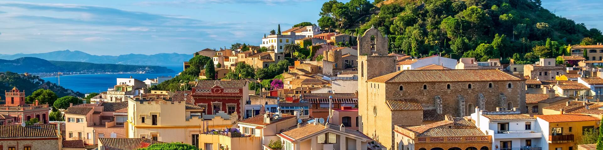 A coastal town with historic buildings, a prominent hilltop fortress, and a view of the sea.