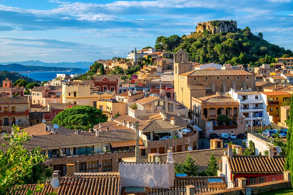 Un pueblo costero con edificios históricos, una fortaleza destacada en una colina y vistas al mar.