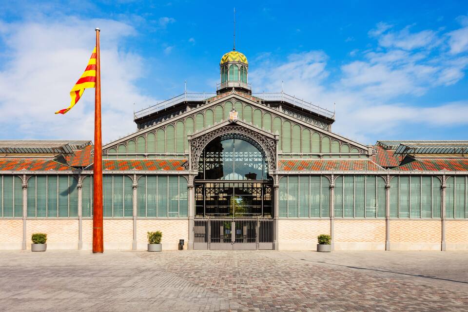 A historic building with a green facade, a large arched entrance, and a flagpole with a striped flag.