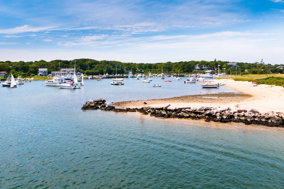 Una marina con barcos amarrados a lo largo de una playa arenosa, rodeada de vegetación y edificios.