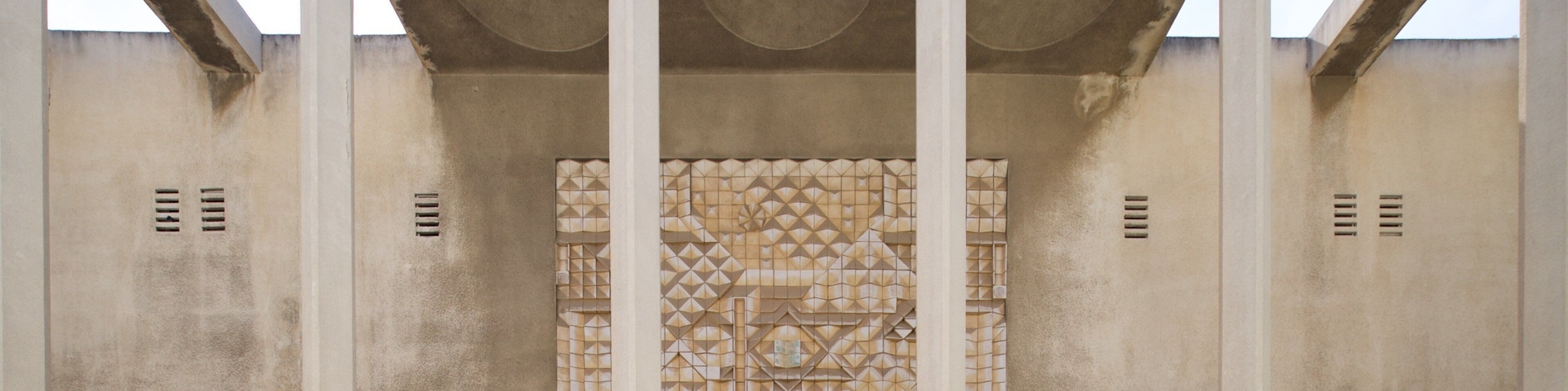 Fachada de edificio con tres arcos y un panel decorativo central.