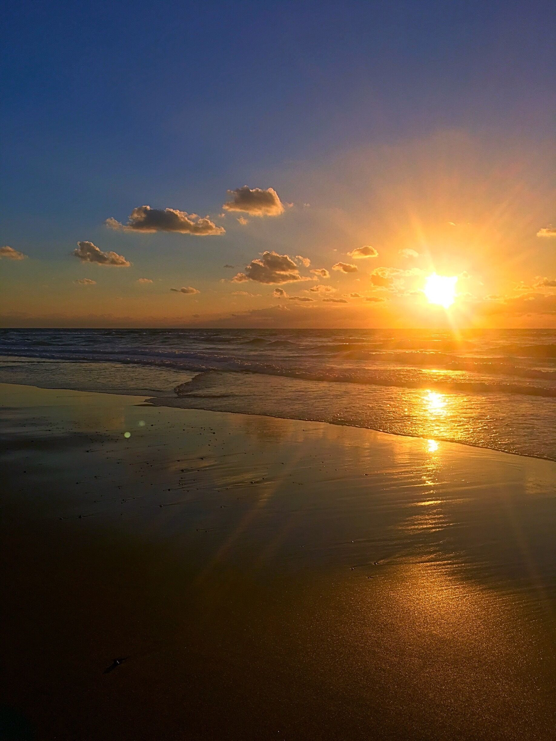 A beach at sunset with the sun reflecting on the wet sand and the ocean.