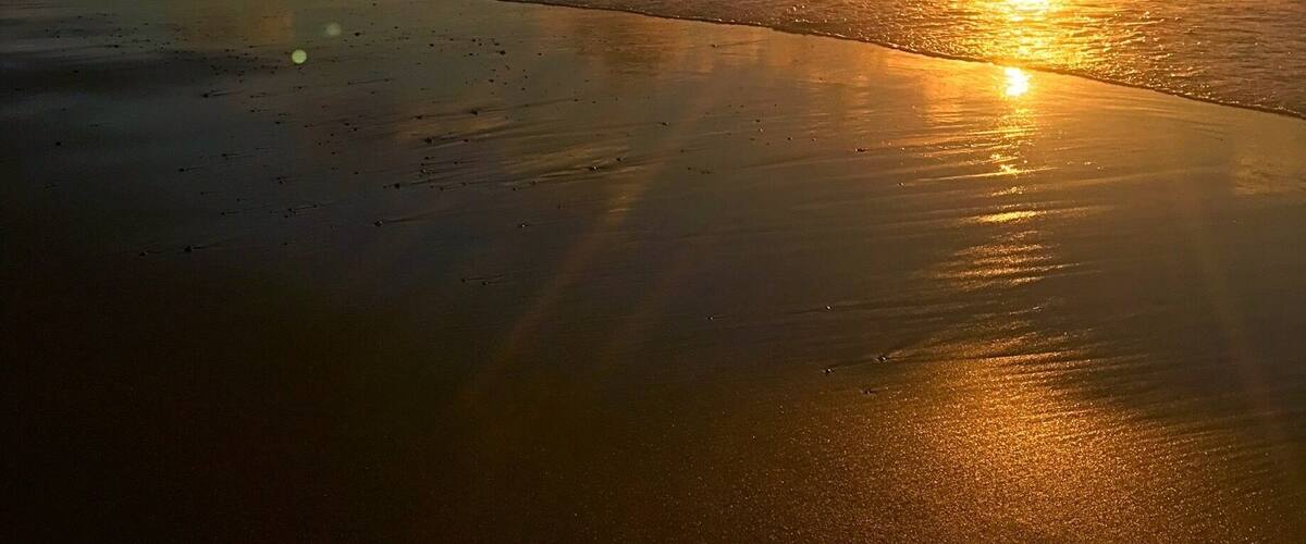 A beach at sunset with the sun reflecting on the wet sand and the ocean.
