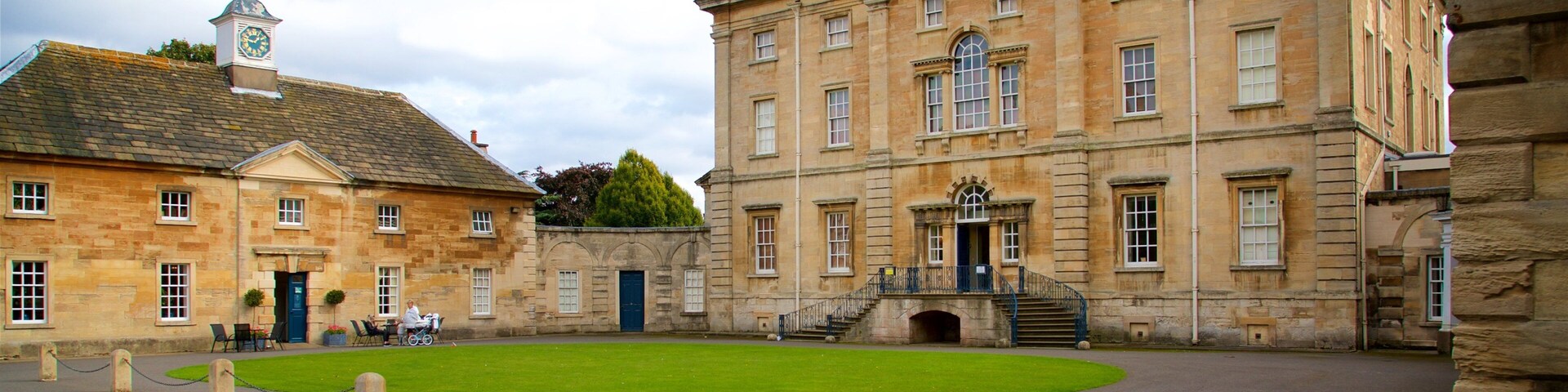 A historic building complex with a central lawn, stone pillars, and a clock tower.