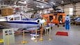 Un hangar con varias aeronaves, incluyendo un avión azul y blanco de Airredale y un helicóptero naranja.