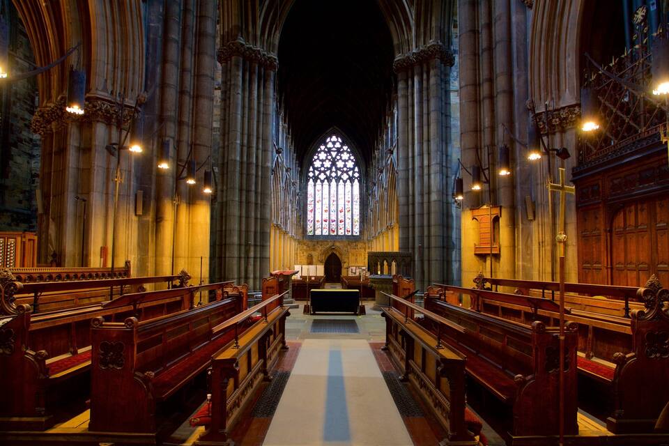 Interior de una catedral con altos techos abovedados, vidrieras de colores y bancos de madera.