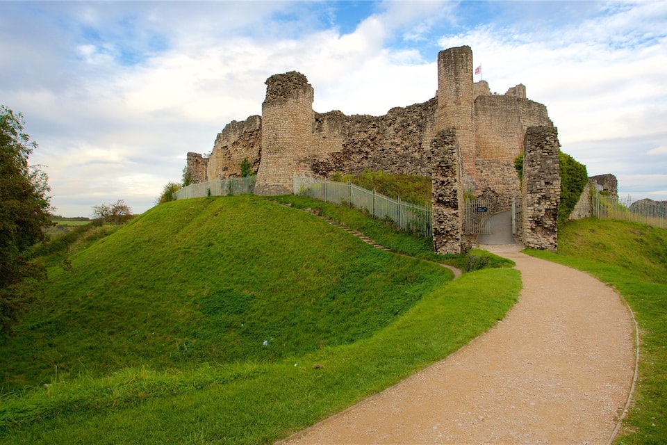 Un château historique, avec une colline verdoyante, un sentier menant à l’entrée et un ciel dégagé.