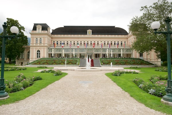 A grand building with a symmetrical facade, a central staircase, and a well-maintained garden with a gravel path leading to the entrance.