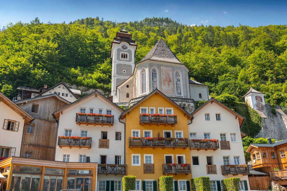 A town with colorful buildings, a church with a bell tower, and a forested hillside.