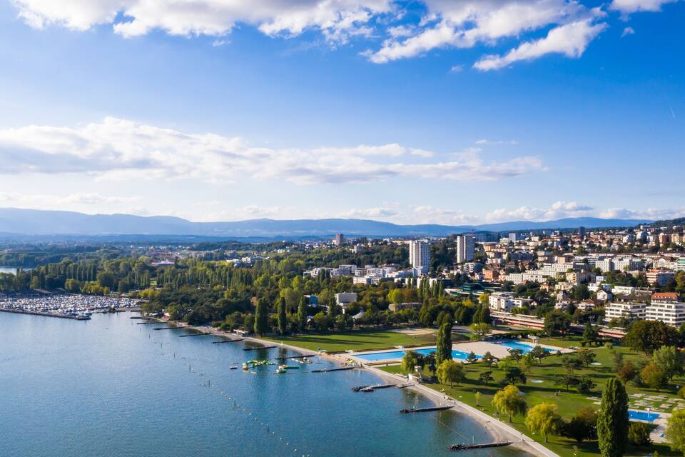 A river with boats, a park, and a cityscape with buildings.