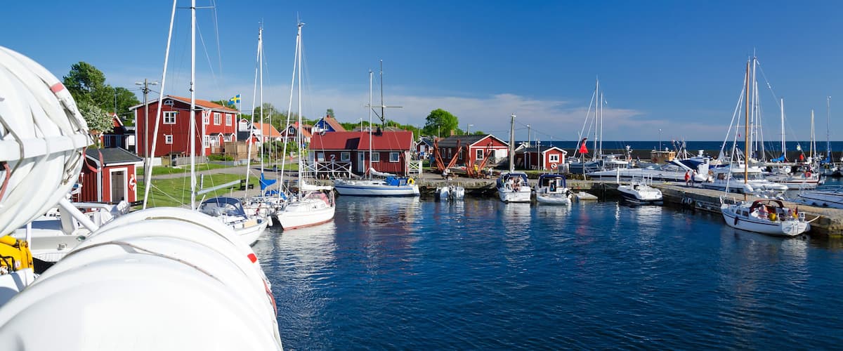 A marina with several boats docked, red houses, and a clear blue sky.