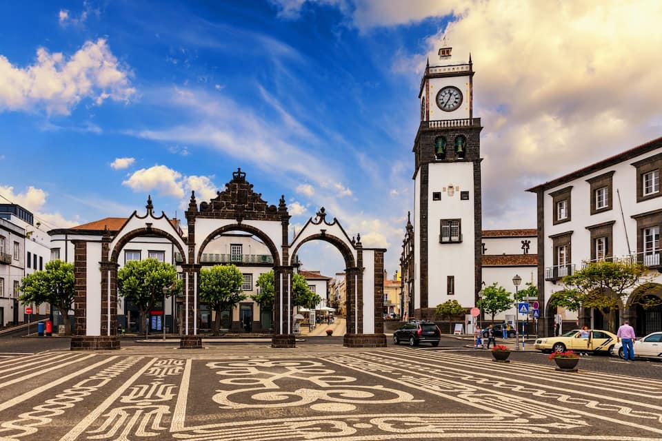 Una plaza histórica con una destacada torre del reloj, arcos y un pavimento con diseños.