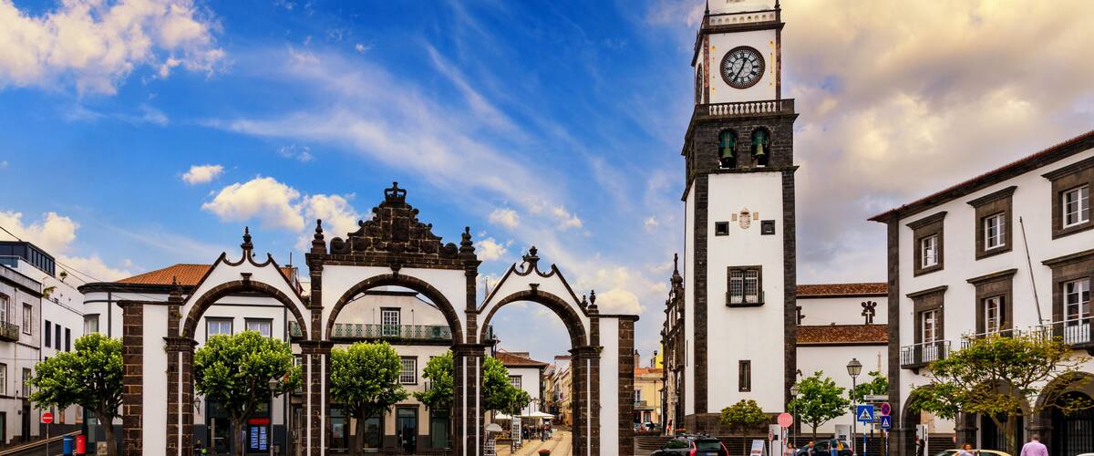 A historic plaza with a prominent clock tower, arches, and a patterned pavement.