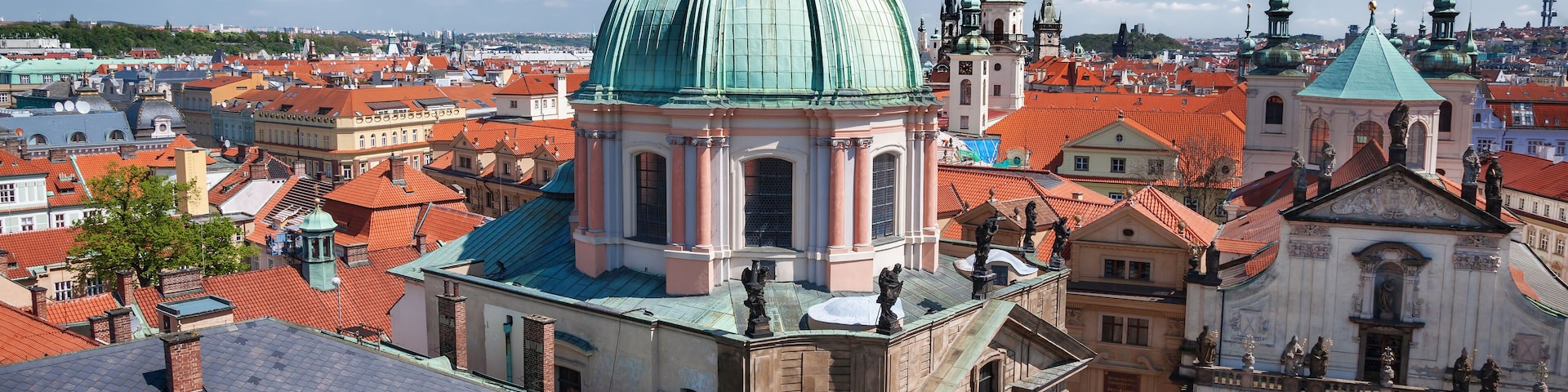 Eine historische Stadtansicht mit einer markanten, grüngekuppelten Kirche, Gebäuden mit roten Dächern und einer belebten Straße mit Autos.