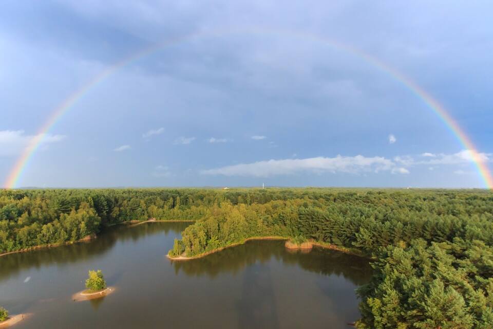 A landscape with two rainbows arching over a forested area and a lake.