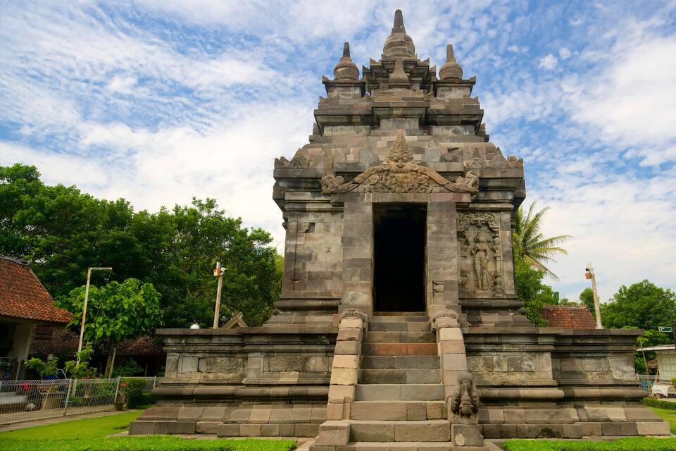 Un tempio in pietra con un portale centrale, affiancato da due leoni in pietra, sullo sfondo di una vegetazione rigogliosa e un cielo parzialmente nuvoloso.