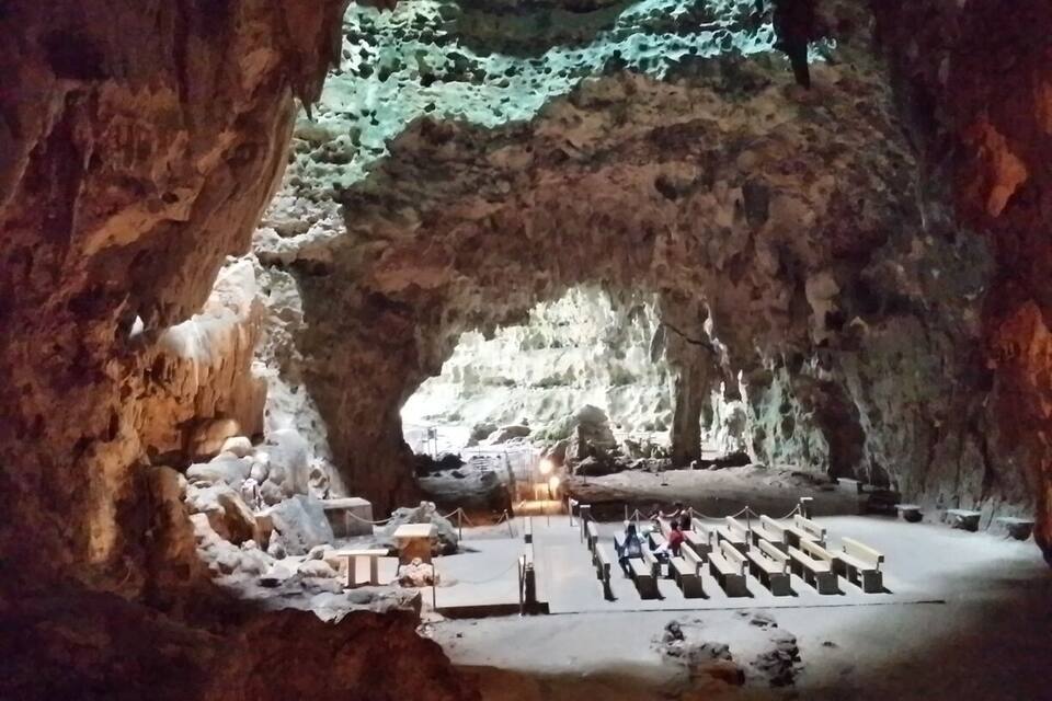 A cave with a large opening, a wooden platform, and a seating area.