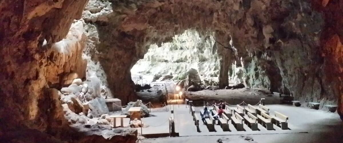 A cave with a large opening, a wooden platform, and a seating area.